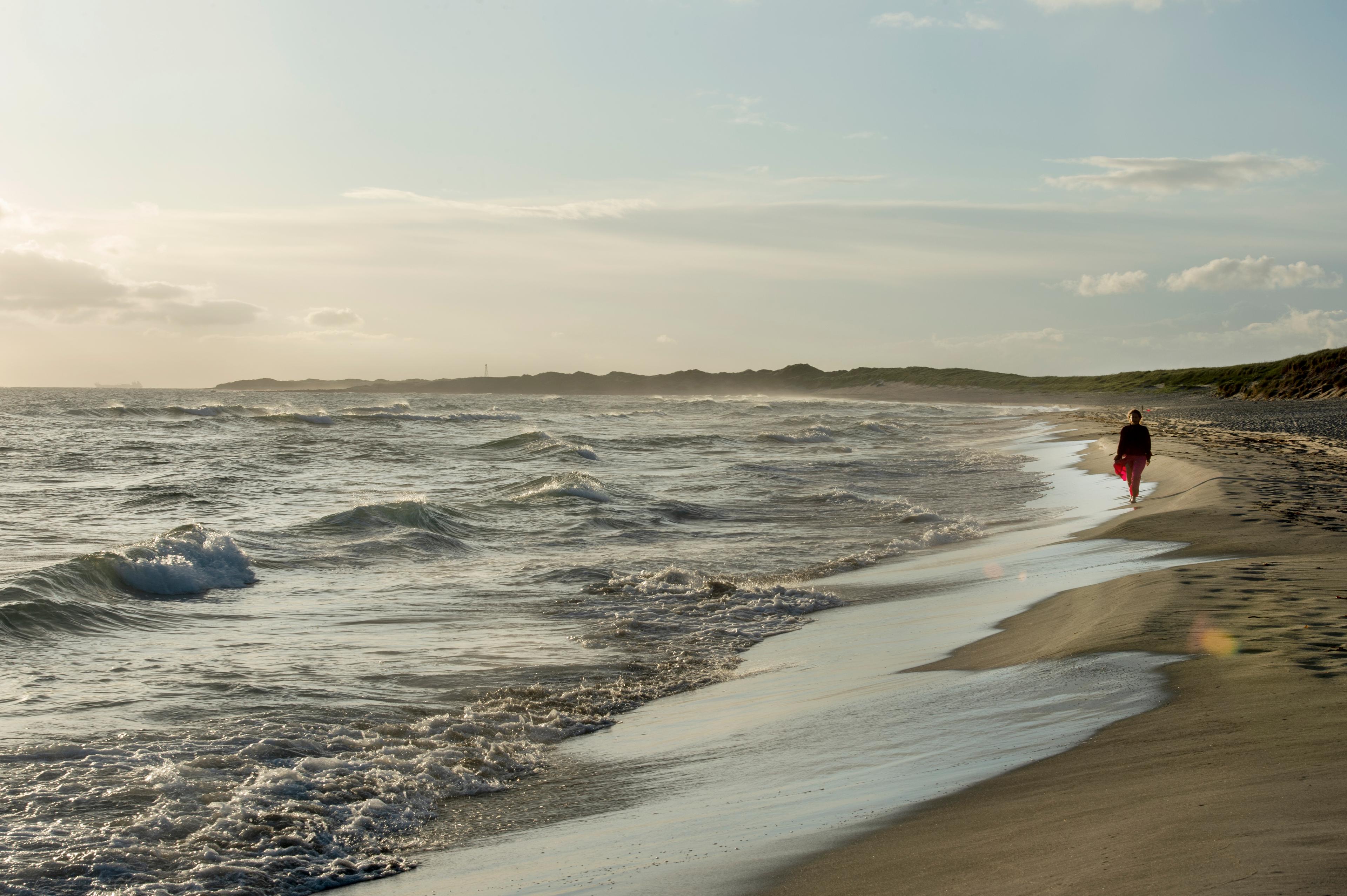 Dame går langs en lang sandstrand