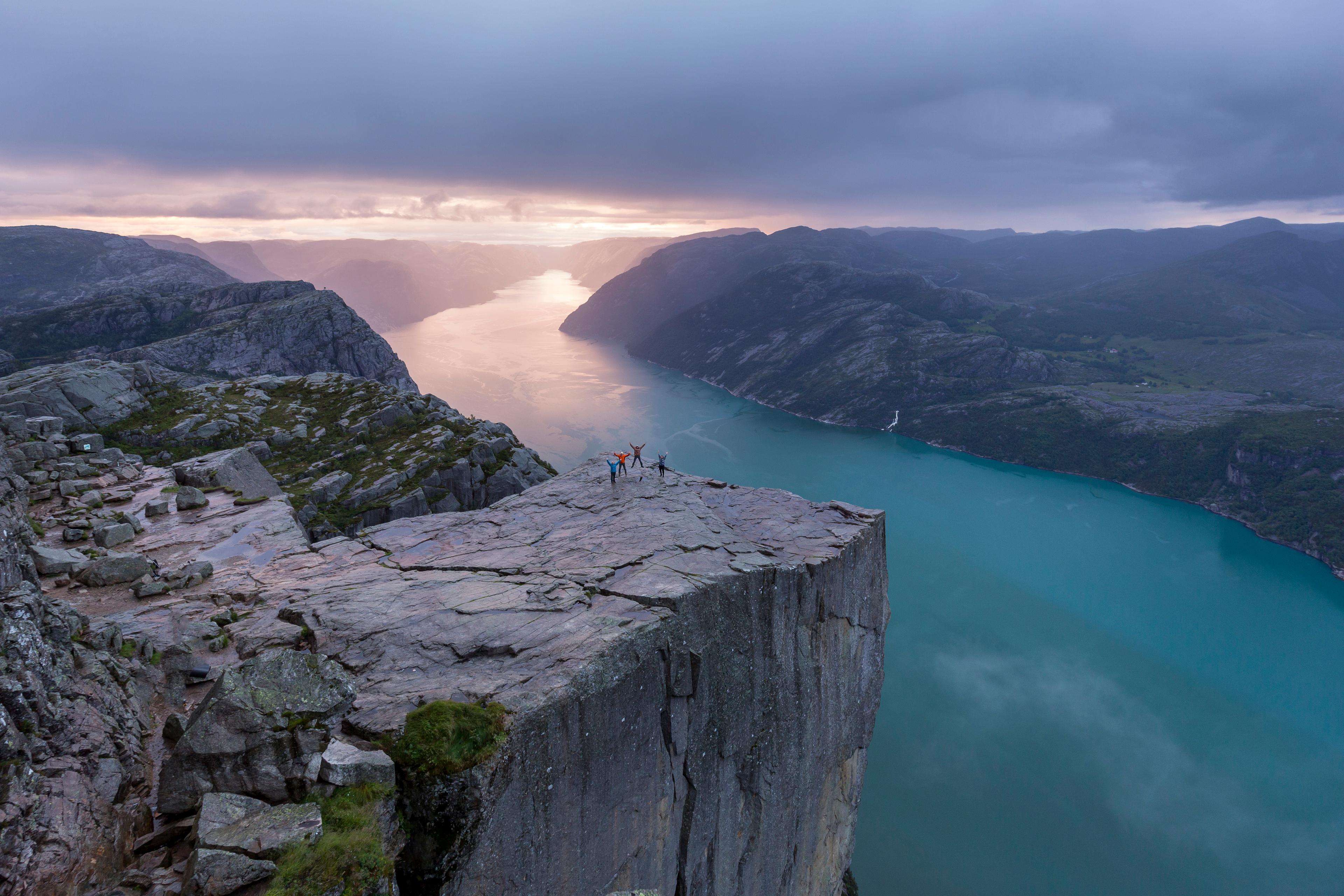 Fire personer som står på Preikestolen i det solen begynner å stige.