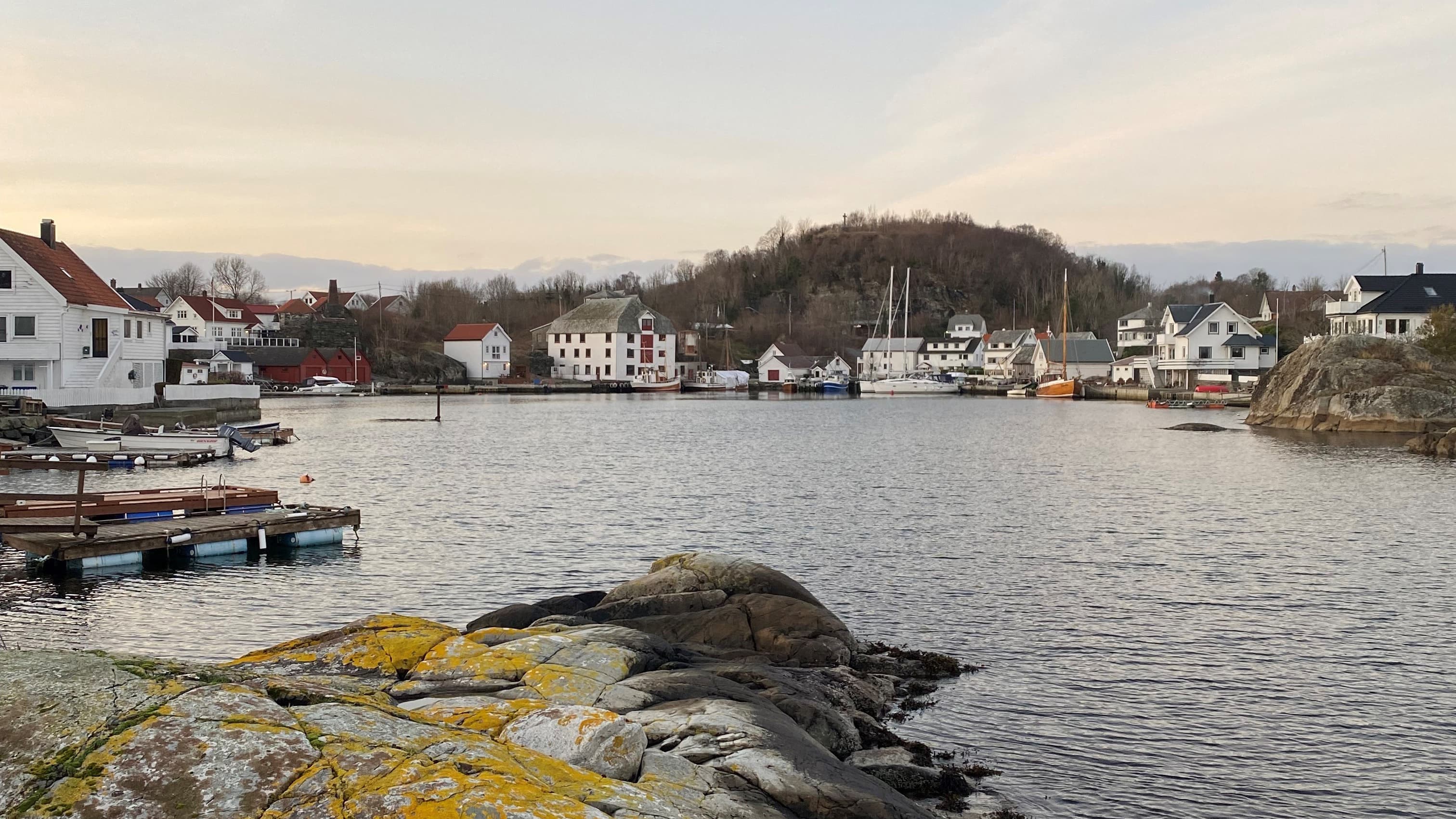 Hus og naust rundt vik, båter på sjøen, flytebrygge.