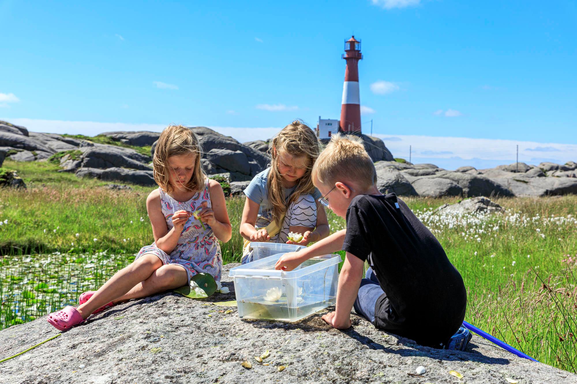 three kids sitting on the rocks in front of Eigerøy lighthouse