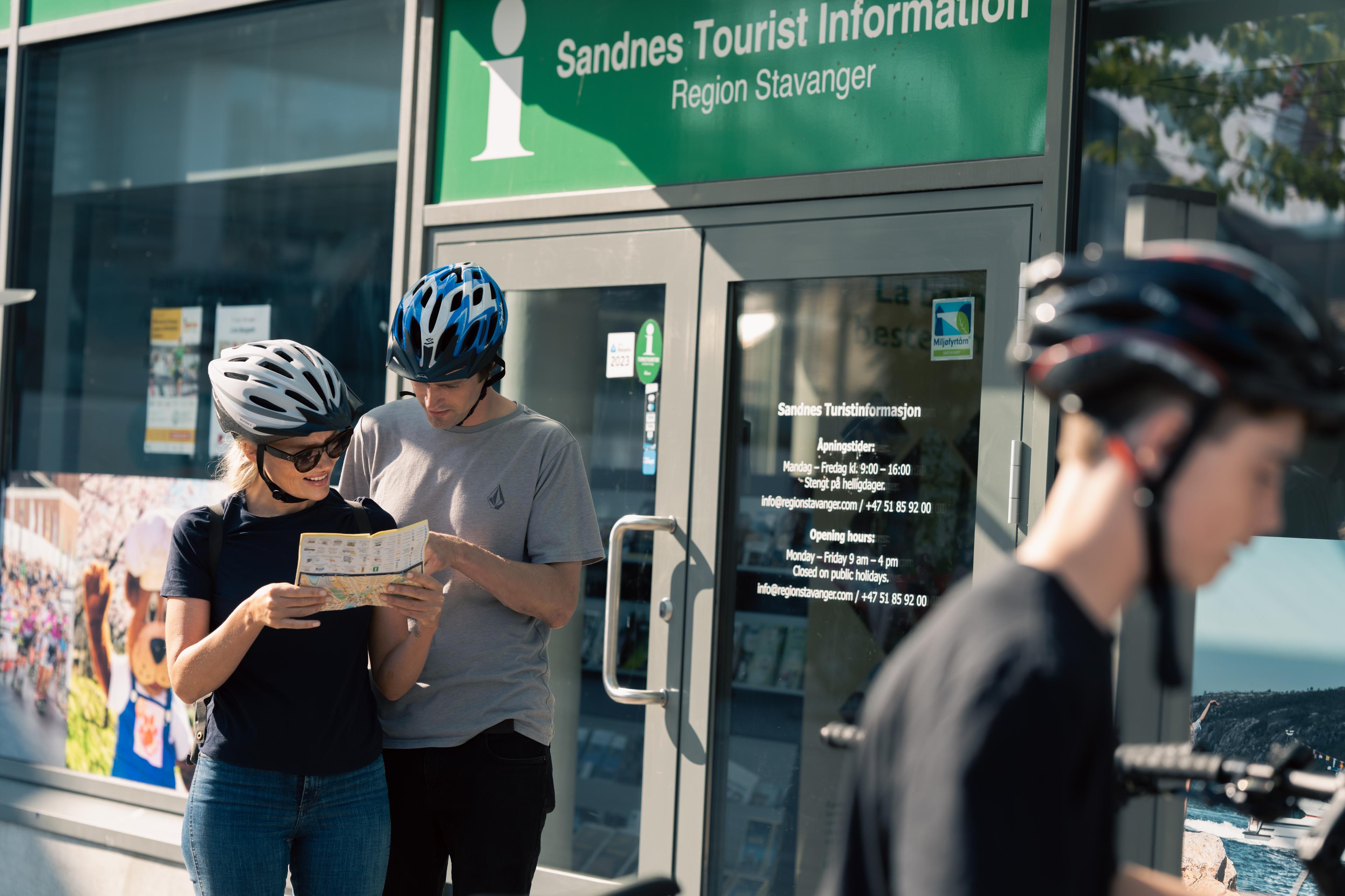 En mann og ei kvinne med sykkelhjelp på hodet ser på kart foran Sandnes turistinformasjon