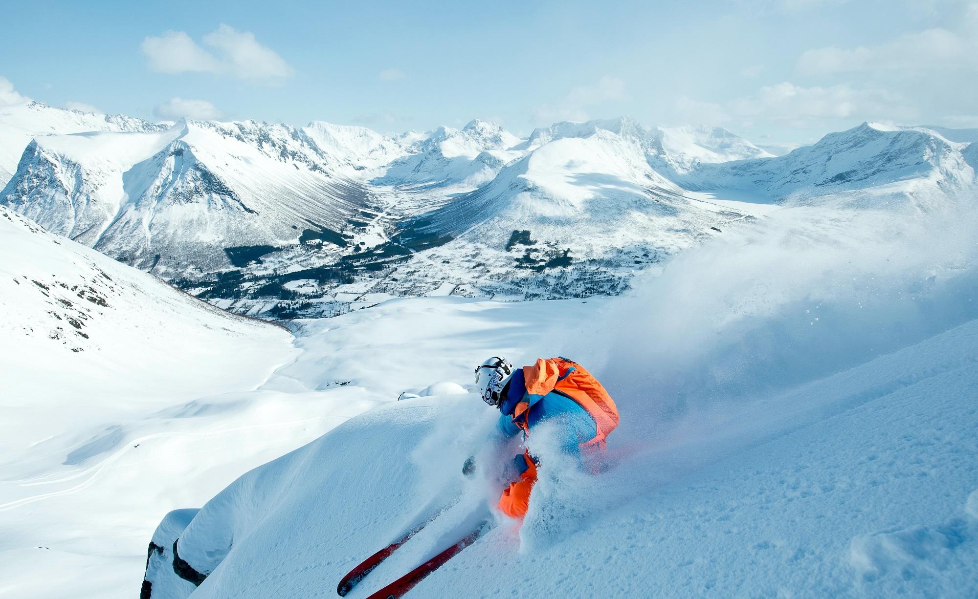 Ein skikøyrar køyrer ned i puddersnøen ved Ørsta skisenter. Sunnmørsalpane i bakgrunnen.