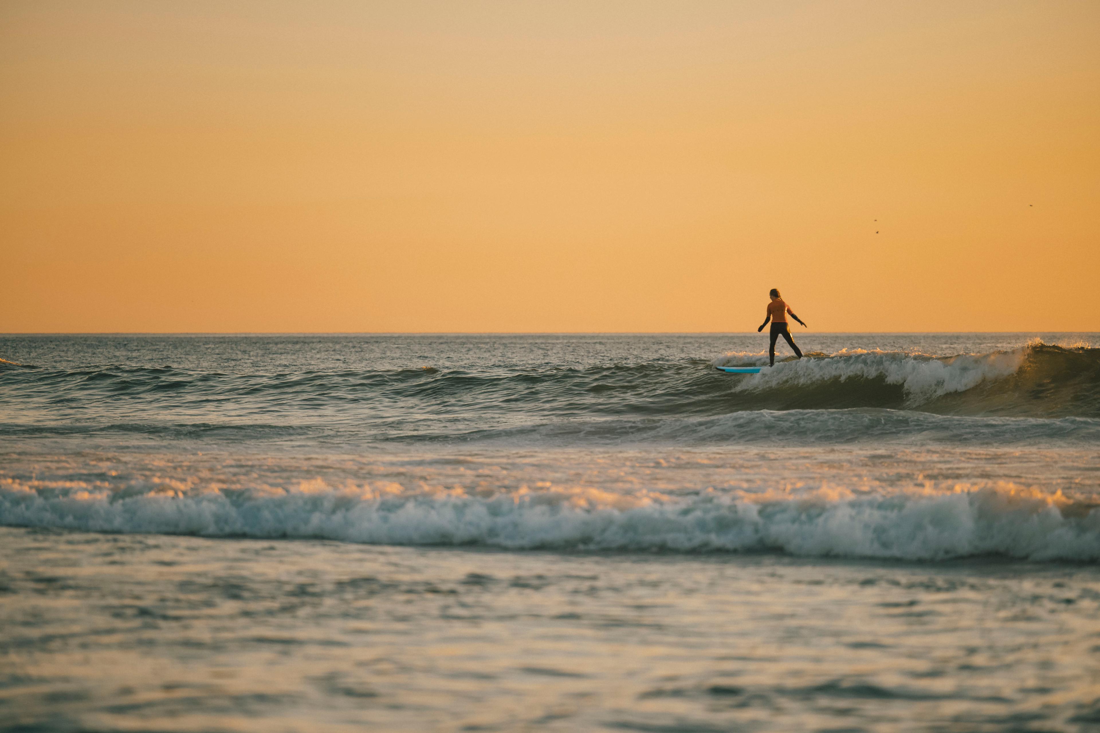 Person on a surfboard on the water. The sky is yellow from the sunset