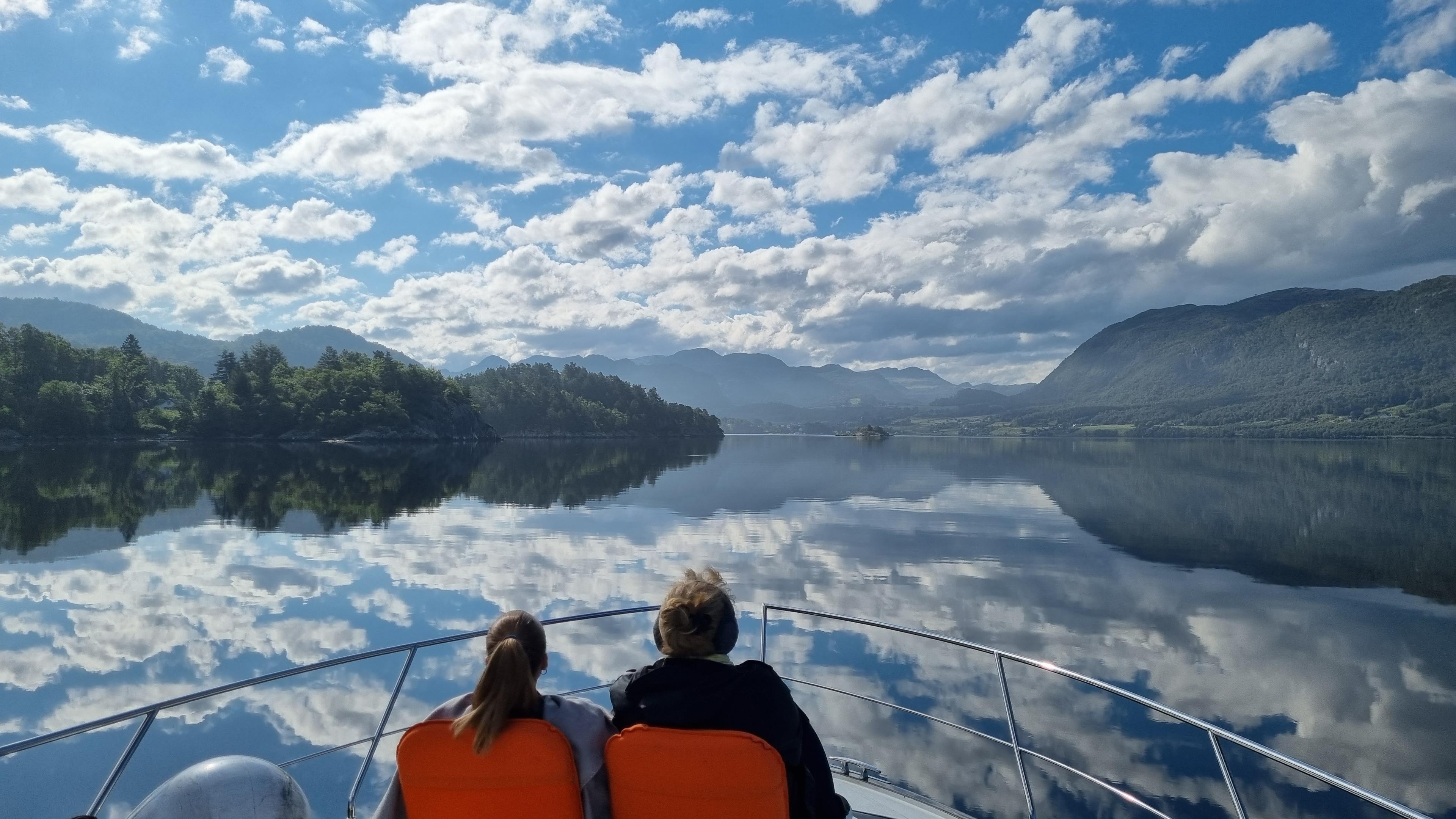 Two people sitting on deck of the boat at a yacht cruise with Private Cruise to the city islands of Stavanger. Blue skies and island scenery