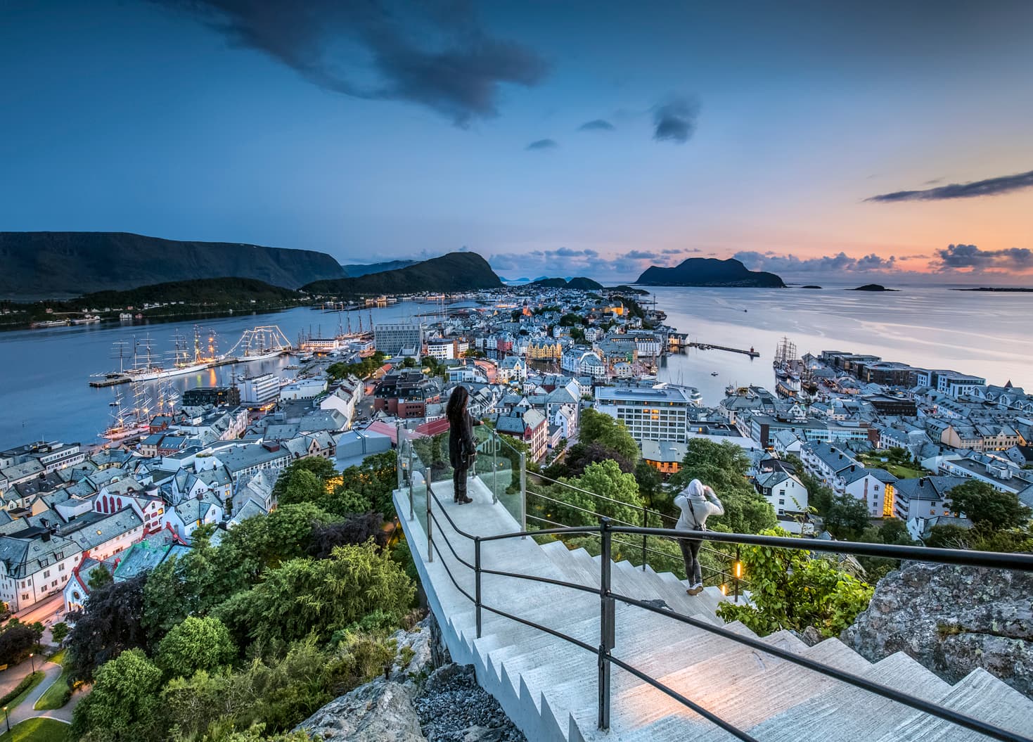 To personer som går opp trapper og som ser på utsikten over Ålesund by.