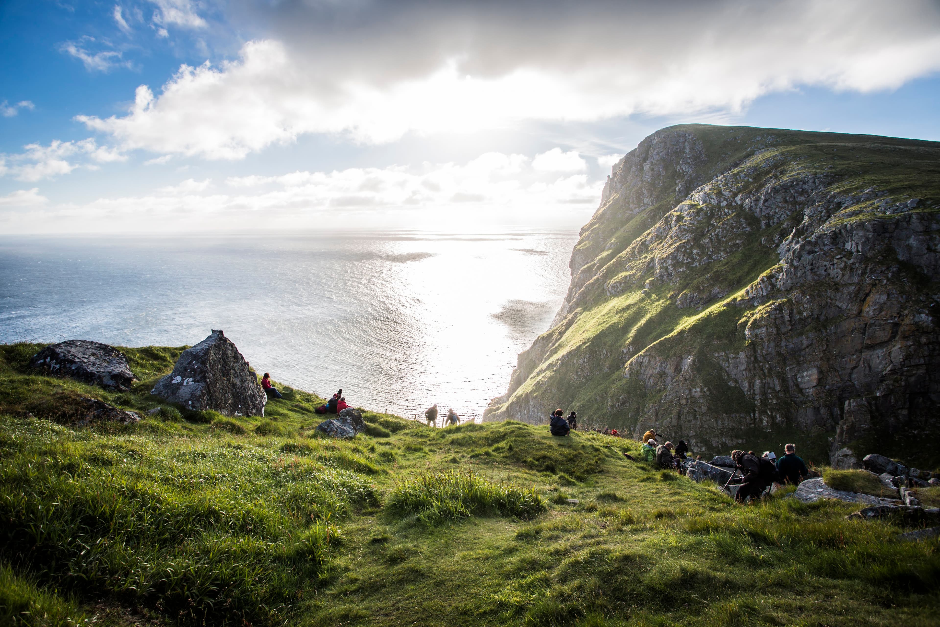 Fuglefjellet på Runde i solnedgang med grøne marker, solnedgang og folk i Lundeura.