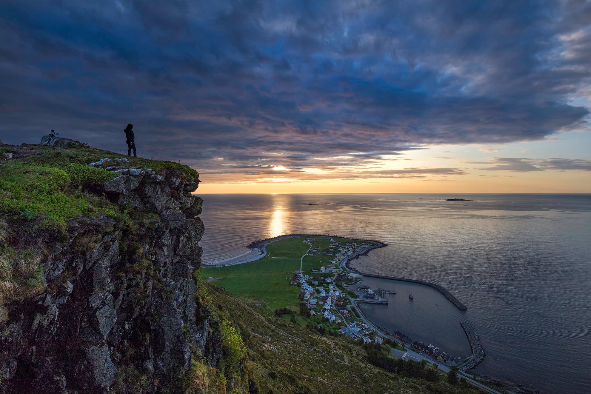 Solnedgang på Alnes sett frå fjellet med person som står framme på fjellet.