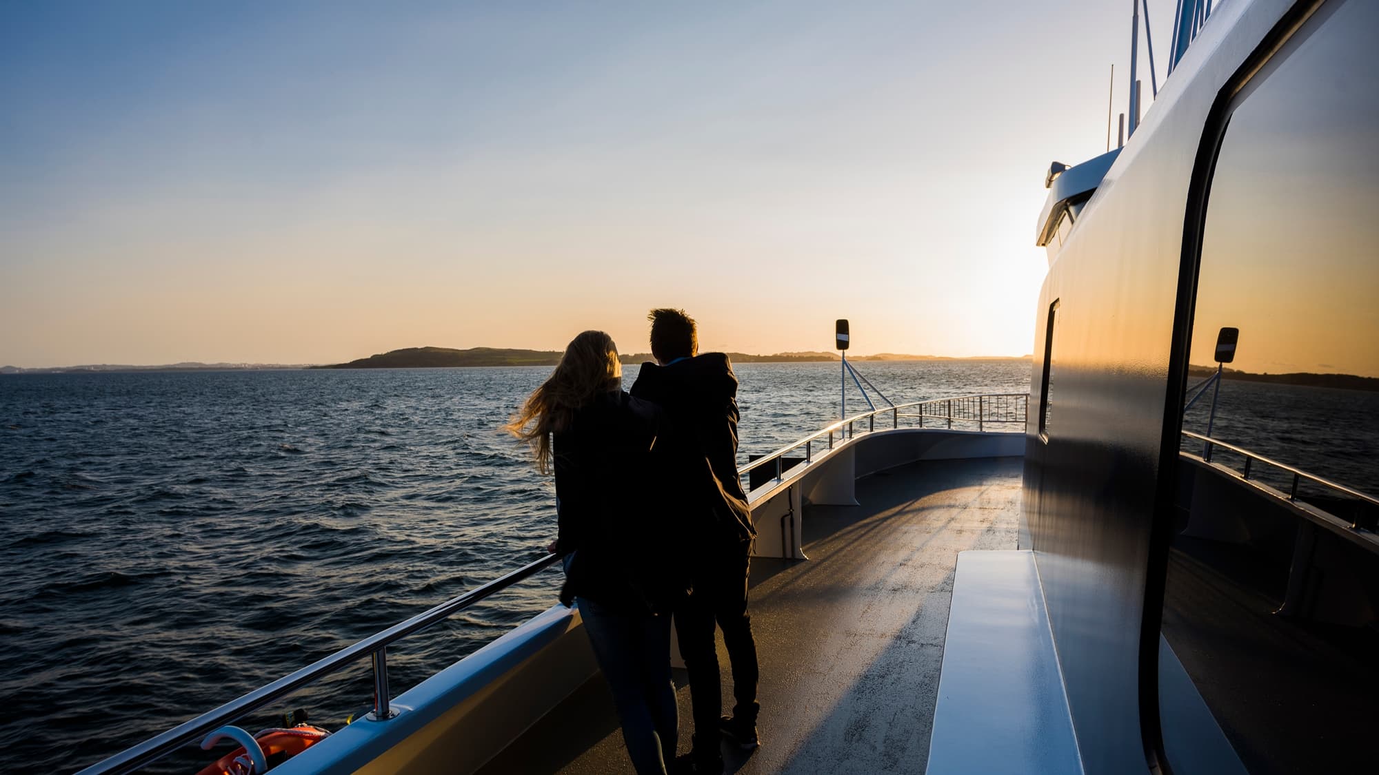 Par står ute på dekk på fjordcruise ved solnedgang