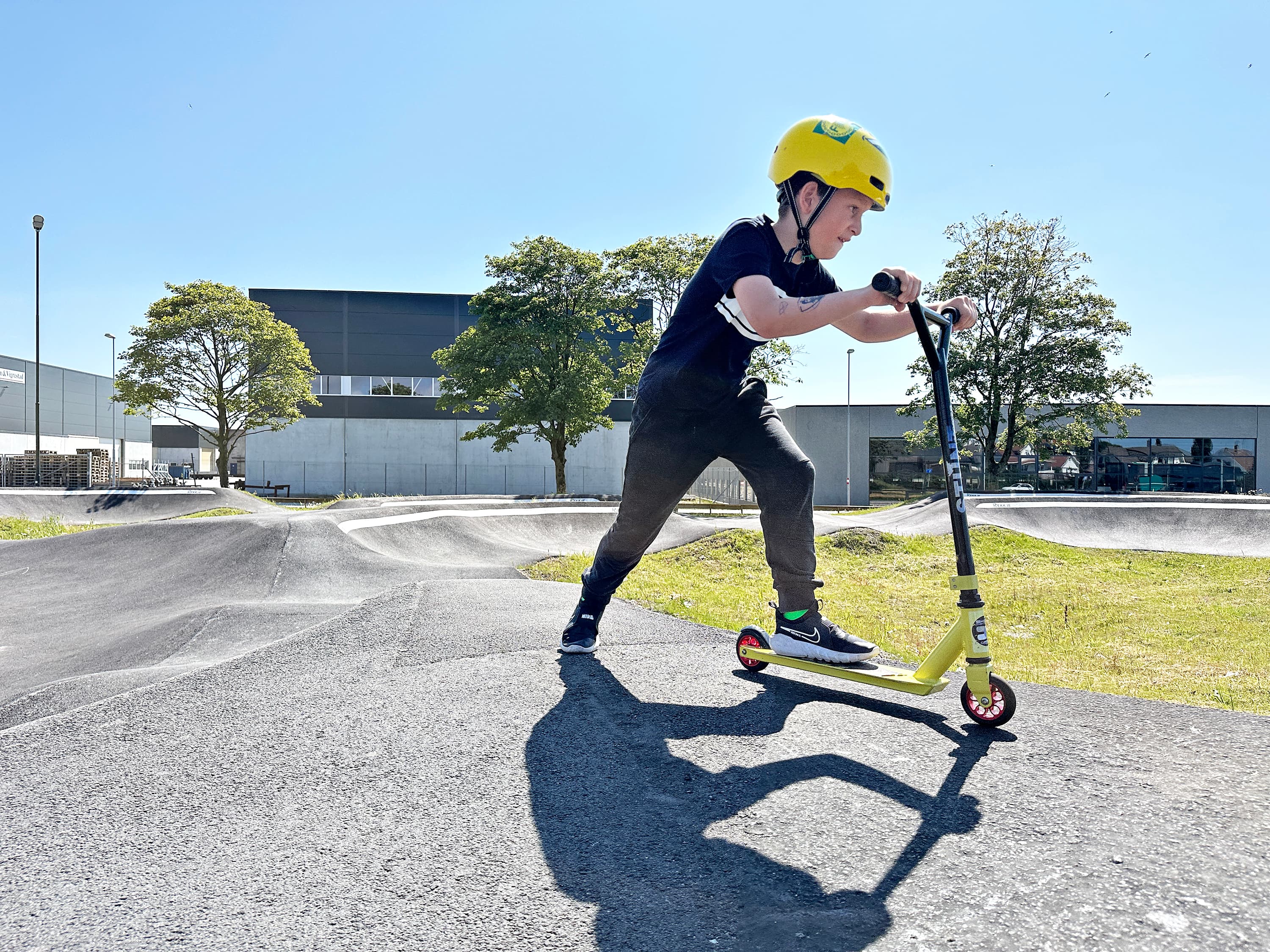 Boy in yellow helmet on a kick scooter on the Pump track course at Vigrestad