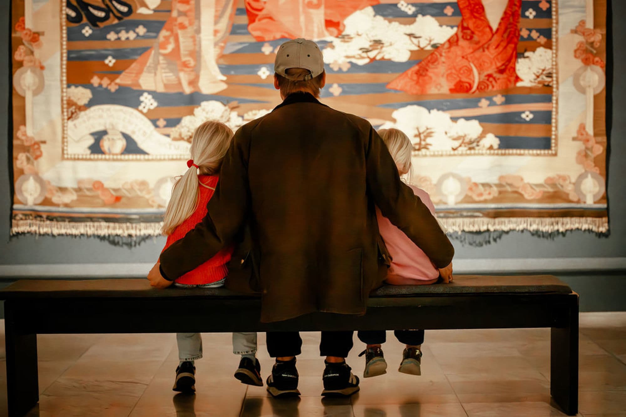 Two girls and man sitting on bench looking at art at an art museum